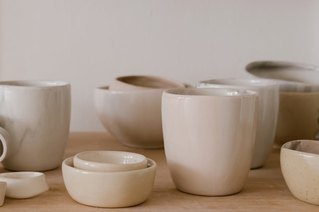 services-01 A collection of handcrafted ceramic bowls and cups in a minimalist style on a wooden table.